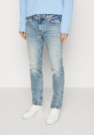 Jeans in denim azzurro chiaro con lavaggio sbiadito e leggere abrasioni. Abbinati a sneakers bianche e a una camicia a maniche lunghe azzurro chiaro.