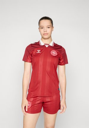 Red soccer kit featuring a striped design with short sleeves, white collar, and sport logo on the chest and shorts. Made from lightweight material.
