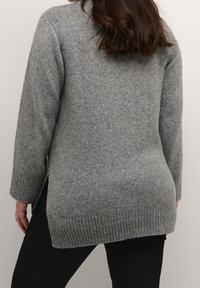 Længere grå strikket sweater med en struktureret overflade, ribkant forneden og slidser i siderne. Har lange ærmer og en løs pasform, der når til midt på hoften.