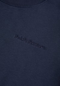 Maglione blu navy con scollatura a coste, caratterizzato da un sottile logo ricamato "PeakPerformance" sul davanti dello stesso colore. Tessuto morbido.