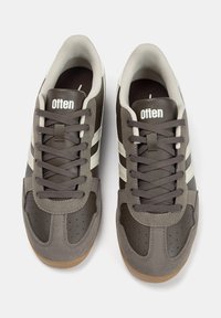 Scarpe sportive marroni con finitura in pelle e scamosciato, dotate di strisce grigio chiaro e suola in gomma texturizzata. Lacci in marrone abbinato.
