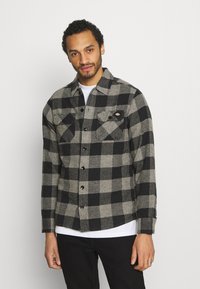 Black and gray plaid flannel shirt with long sleeves, button closure, two chest pockets, and a rounded hemline.