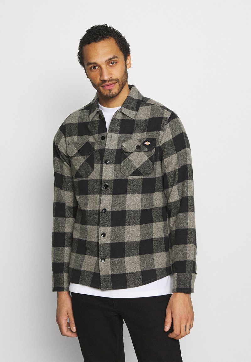 Black and gray plaid flannel shirt with long sleeves, button closure, two chest pockets, and a rounded hemline.