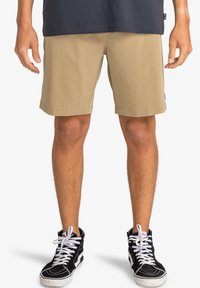 Pantalones cortos a cuadros en color beige con un ajuste relajado, puños dobladillos y bolsillos laterales, combinados con zapatillas altas negras con cordones blancos.