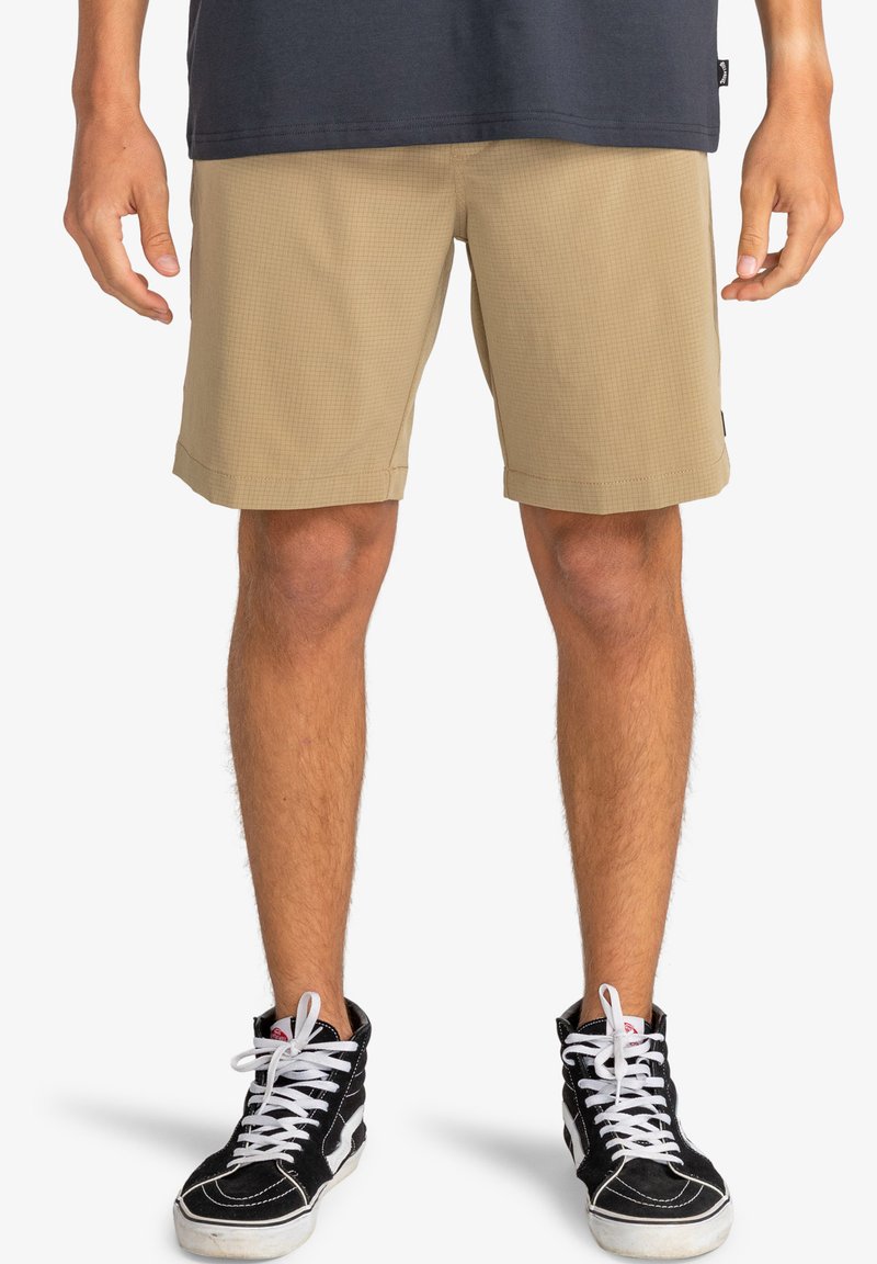 Pantalones cortos a cuadros en color beige con un ajuste relajado, puños dobladillos y bolsillos laterales, combinados con zapatillas altas negras con cordones blancos.