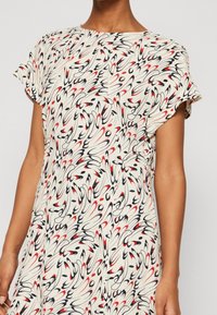 Vestido de manga corta en tejido ligero, con un fondo beige que presenta remolinos de patrones abstractos en rojo, negro y azul marino.