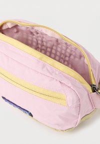 Μικρό τσαντάκι σε ροζ και μπεζ χρώμα με κίτρινες φερμουάρ, μερικώς ανοικτό που δείχνει το εσωτερικό επένδυμα σε ανοιχτό ροζ χρώμα.