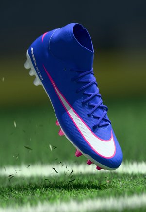 Scarpetta da calcio blu con collo alto, con uno swoosh bianco e rosa, tomaia testurizzata e tacchetti rosa, sollevata sopra l'erba.