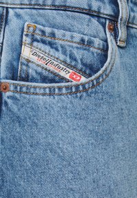 Ljust blå denimjeans med en framficka som har en vit och röd etikett med texten "Diesel Industry Denim Division" och kontrasterande gul tråd.