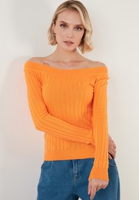 Pulover ribbed portocalie fără umeri, cu mâneci lungi. Textură moale, design ajustat și tiv drept. Asortat cu blugi bleumarin.