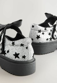 Chaussures à paillettes noires et argentées avec des motifs d'étoiles, dotées d'une douce sangle en tissu noir et d'une semelle épaisse en caoutchouc noir.