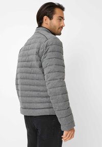 Grå puffjakke med quiltet design, lange ærmer, høj krave og en glat overflade. Har subtile syninger og en tætsiddende silhuet.