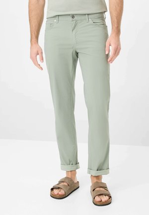 Pantaloni slim-fit verde chiaro con una sottile texture; presentano cinque tasche, passanti per cintura e risvolti, abbinati a sandali marroni.