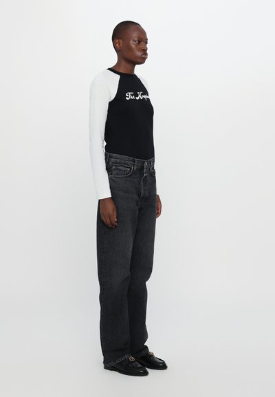 Top de manga larga blanco y negro con el texto "The Koppel", combinado con vaqueros oscuros de cintura alta y mocasines negros, con un acabado pulido.