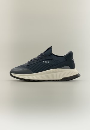 Granatowy niski sneaker z teksturowaną dzianą cholewką, białą grubą żeberkowaną podeszwą, czarną podeszwą zewnętrzną i logo "BOSS" na boku i pasku na pięcie.