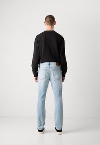 Schwarzer Sweatshirt und hellblaue Jeans an einer Person, mit einem braunen Lederpatch am Bund und zwei sichtbaren Gesäßtaschen.