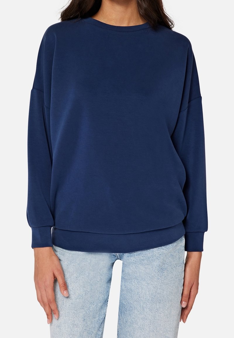 Felpa blu navy, vestibilità comoda, scollo tondo, maniche lunghe con polsini a coste, texture morbida, indossata con jeans azzurri.