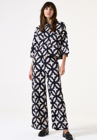 Zweiteiliges Outfit mit einem schwarz-creamfarbenen Zickzackmuster. Die Jacke ist eine kurz geschnittene Jacke, und die weit geschnittenen Hosen haben ein passendes Design.