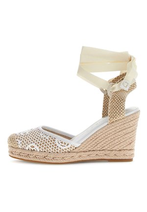 Beige gewebte Keil-Espadrille mit weißer Spitzenverzierung, Riemen zum Umschlagen am Knöchel und einem kleinen dekorativen "G"-Anhänger am Fersenriemen.