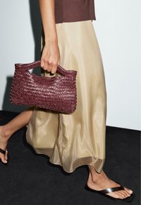 Woven burgundy handbag with a curved handle, paired with a flowing beige satin skirt. The skirt has a slight sheen and a relaxed fit.