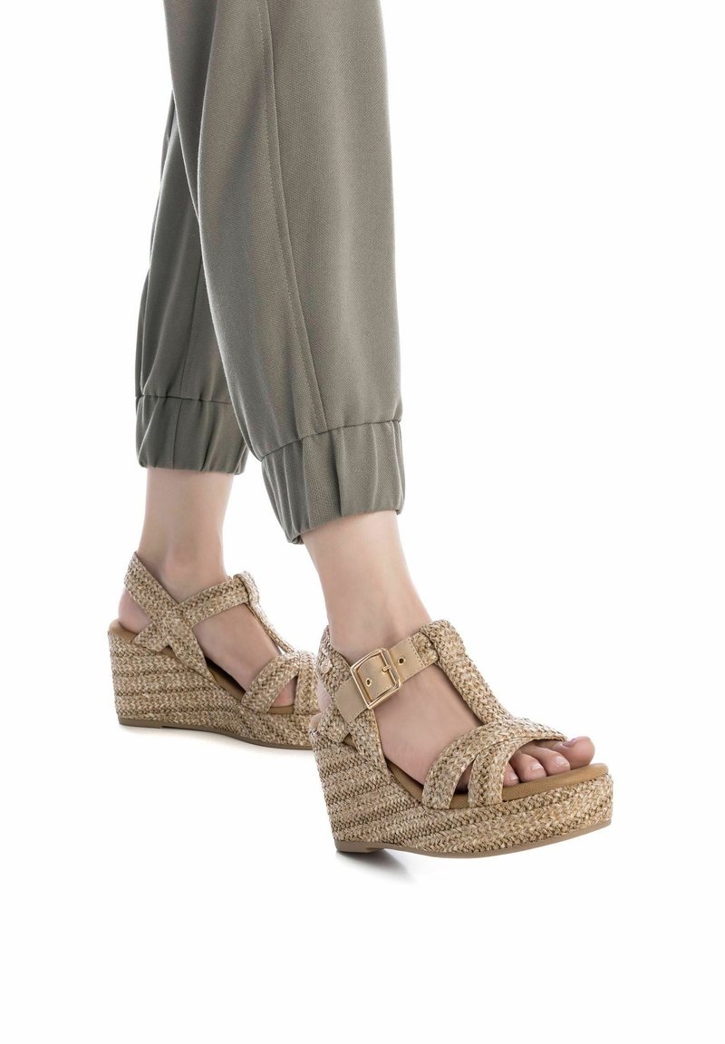Sandalias de cuña con un upper de paja trenzada y textil beige, con correas en el tobillo ajustables y una suela de plataforma texturizada.