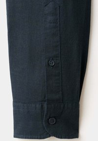 Manche de chemise en tissu foncé avec un poignet boutonné et une patte visible avec un bouton fermé.