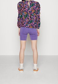 Blusa floreale viola con maniche a sbuffo, pantaloni da bici viola abbinati a calze bianche e sneakers con accenti arancioni.