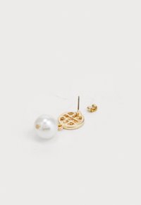 Goudkleurige oorbellen met een grote witte parel en een decoratieve cirkelvormige accent met uitgesneden patronen. Inclusief een druksluiting.