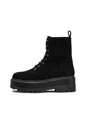 Black suede ankle boot with platform sole, lace-up front, and pull tab at the back. Textured surface and chunky tread pattern on sole.