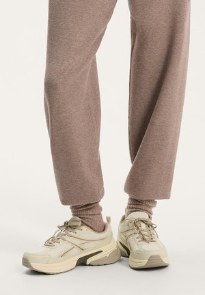 Pantalon marron coupe décontractée associé à des chaussettes épaisses assorties et des baskets beiges épaisses à lacets.