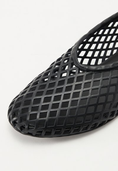 Black flat shoe made of molded material featuring an open lattice design. The toe is rounded with a smooth, non-slip interior texture.