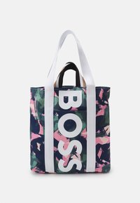 Tote bag met een meerkleurig abstract patroon in groen, roze en marineblauw. Beschikt over grote witte letters en witte hengsels.