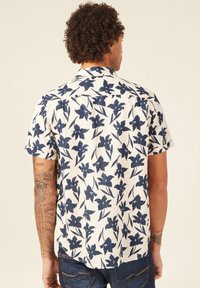 Lyhythihainen kermavärinen paita, jossa on tummansininen kukkakuosi. Varustettu kauluksella, rento leikkaus ja suora helma.