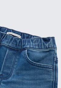 Denim džinsai su elastinga juosmens juosta, vidutinės mėlynos spalvos, su priekiniu kišeniu ir etikete, kurioje nurodyta "pagaminta iš perdirbtų medžiagų."