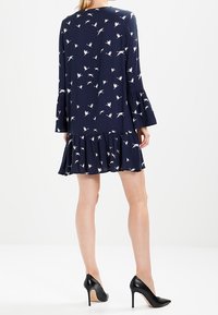 Navy blue dress with white bird prints, long bell sleeves, and a flared hem. Worn with black high-heeled shoes. Soft fabric texture.