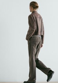 Brun cropped læderjakke, gråstribet top og løstsiddende grå jeans. Modellen går og viser det afslappede fit og de afdæmpede farver i outfittet.