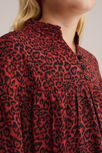Sarkans un melns leopardu raksta blūze ar viļņotu apakšmalu, pogu detaļām un savilktu augšdaļu. Mīksta auduma tekstūra un brīva piegriezuma.