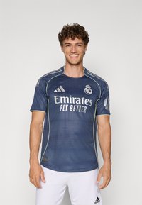 Maglietta sportiva blu scuro con collo tondo, maniche corte e dettagli gialli. Presenta il logo "Emirates Fly Better" e lo stemma del club sul petto.