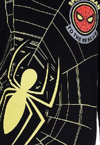 Czarna tkanina z ilustracją żółtego pająka, wzorem sieci i okrągłym znakiem Spider-Mana z czerwonymi i żółtymi detalami.