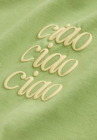 Tissu vert avec texte crème en relief « ciao » répété trois fois en écriture cursive.