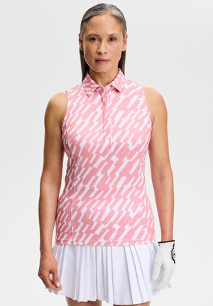 Vrouw die een mouwloze roze golfshirt met patroon draagt, een witte geplooide rok en een witte golfhandschoen aan de rechterhand tegen een effen achtergrond.