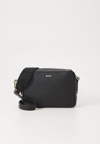 Borsa a tracolla in pelle nera con finitura testurizzata, caratterizzata da un logo in tono oro e un cinturino regolabile con branding in rilievo. Chiusura con zip.