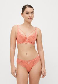 Coral lace alusvaateset, jossa on kevyt rintaliivisetti säädettävillä olkaimilla ja koristeellinen nauha, yhdistettynä yhteensopiviin matalavyötäröisiin alushousuihin.
