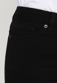 Levi's jeans de mezclilla negra con un diseño ajustado, que cuentan con un pequeño bolsillo frontal, costuras sutiles y herrajes metálicos en la cintura.