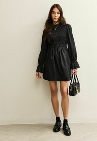 Czarna sukienka z marszczonym gorsetem, długimi bufiastymi rękawami i rozszerzanymi mankietami. W połączeniu z elegancką czarną torebką oraz błyszczącymi loafersami.