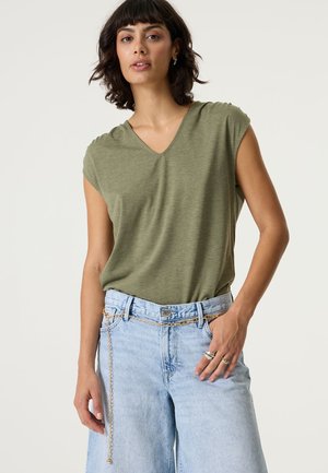 Grünes T-Shirt mit V-Ausschnitt und kurzen Ärmeln aus einem weichen, leichten Stoff. Kombiniert mit hellblauen Jeansshorts, die mit einem Kettenakzent am Gürtel versehen sind.