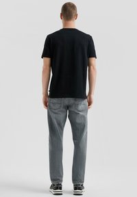 Schwarzes Baumwoll-T-Shirt mit Rundhalsausschnitt, kombiniert mit hellgrauen Denim-Jeans. Die Jeans haben eine verblichene Textur und Gesäßtaschen.