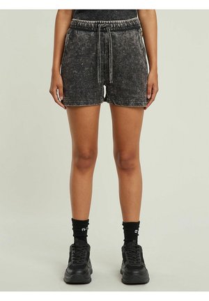 Person wearing black acid-wash shorts with drawstring, black socks, and black sneakers standing against a plain light background.