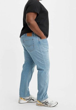 Vaqueros de mezclilla azul claro con corte de pierna recta, con un parche de cuero en la parte trasera y dos bolsillos traseros. Combinados con una camiseta negra y zapatillas.