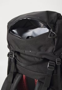 Svart tursekk med delvis åpen toppglidelås, justerbare stropper og polstret bakpanel med røde mesh-detaljer.